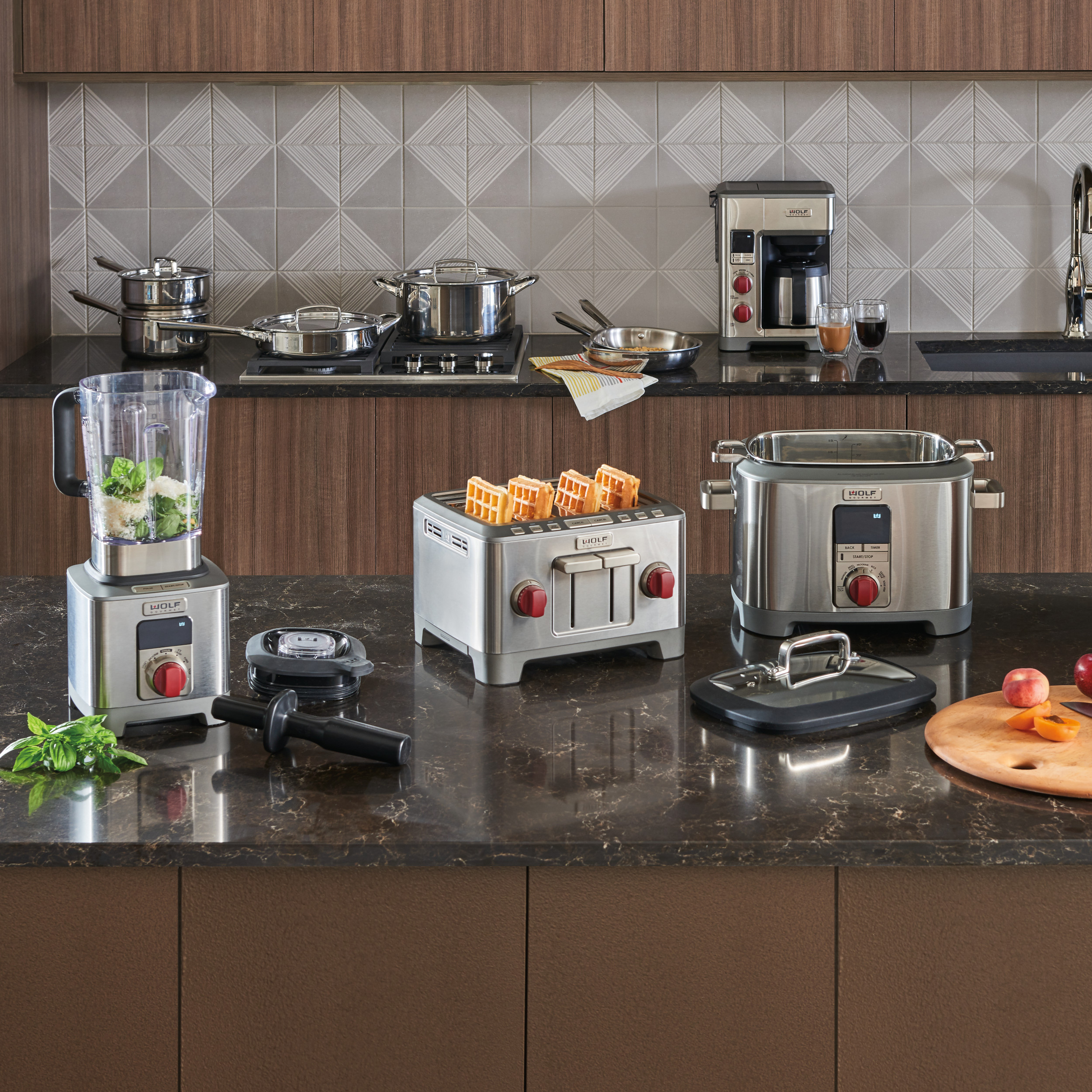 Group shot of Wolf Gourmet Precision Blender, Four-Slice Toaster, and Multi-Function Cooker, with Coffee Maker and Cookware in background