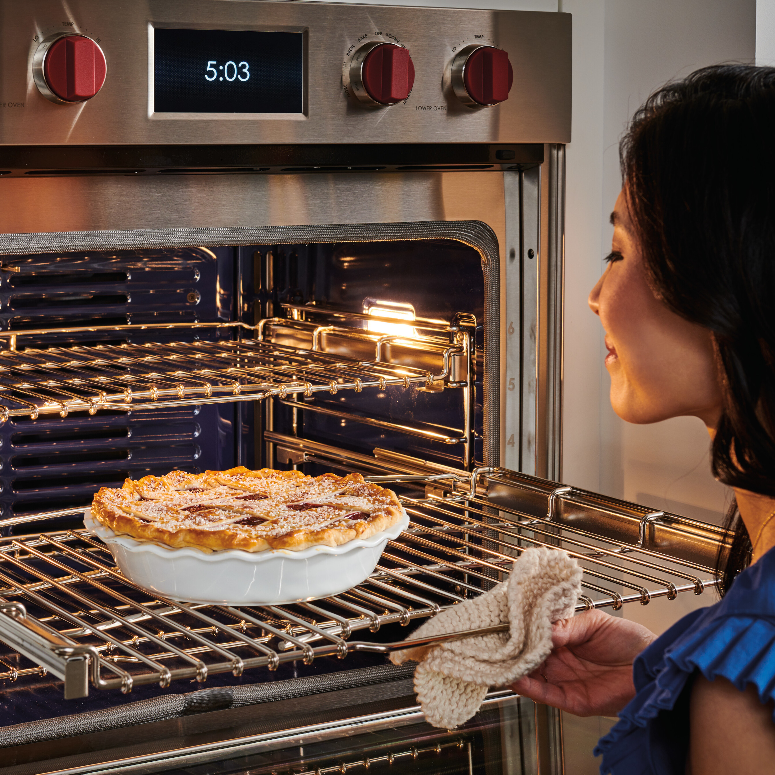 A woman takes a pie out of a Wolf oven, demonstrating the quality and hospitality with which Shoreline Appliance Service is synonymous..